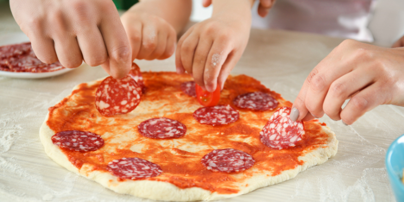a pizza on the counter in the process of being made by a family